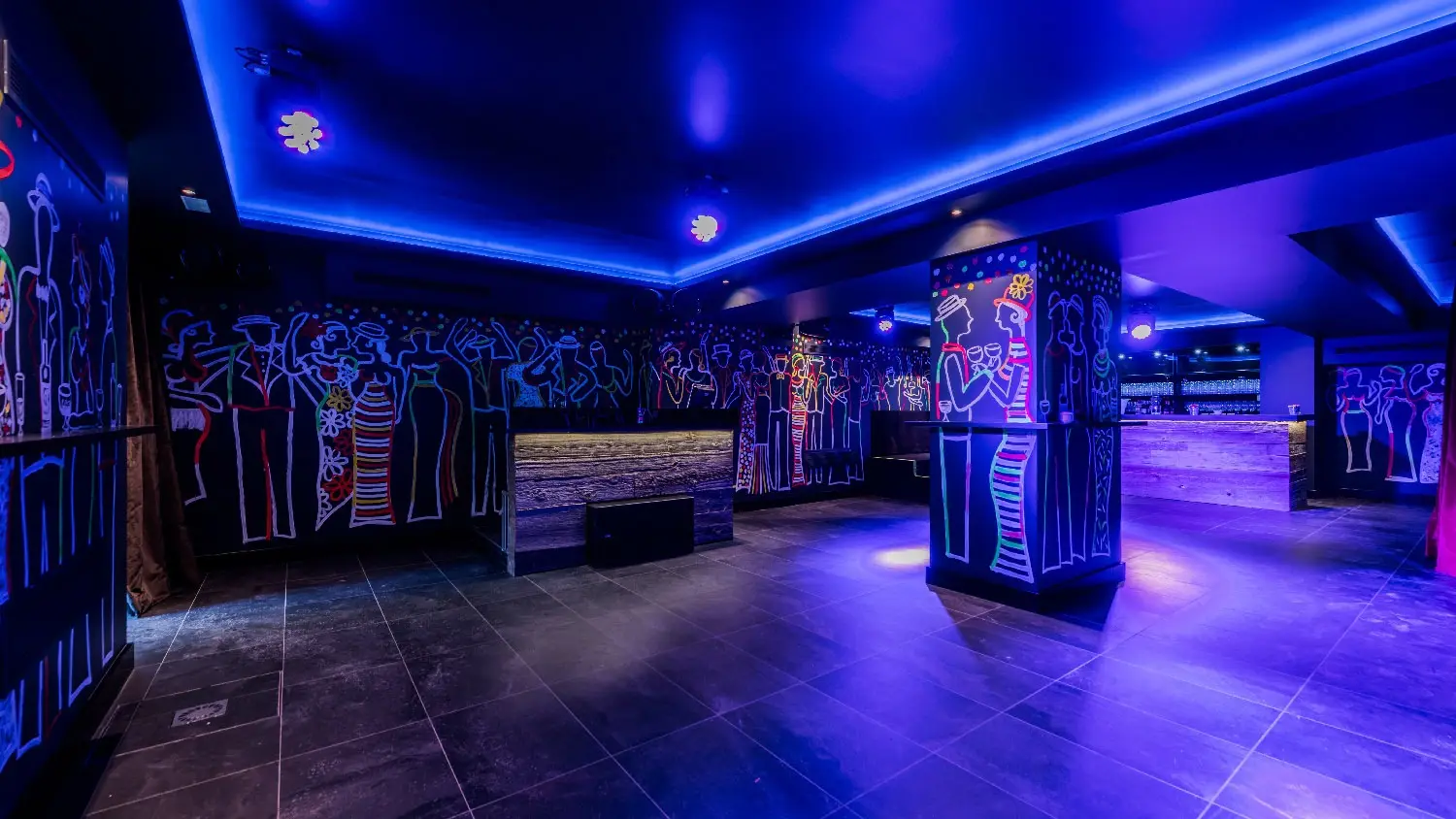 La discoteca del sótano con luz azul, columnas y paredes cubiertas de dibujos de figuras