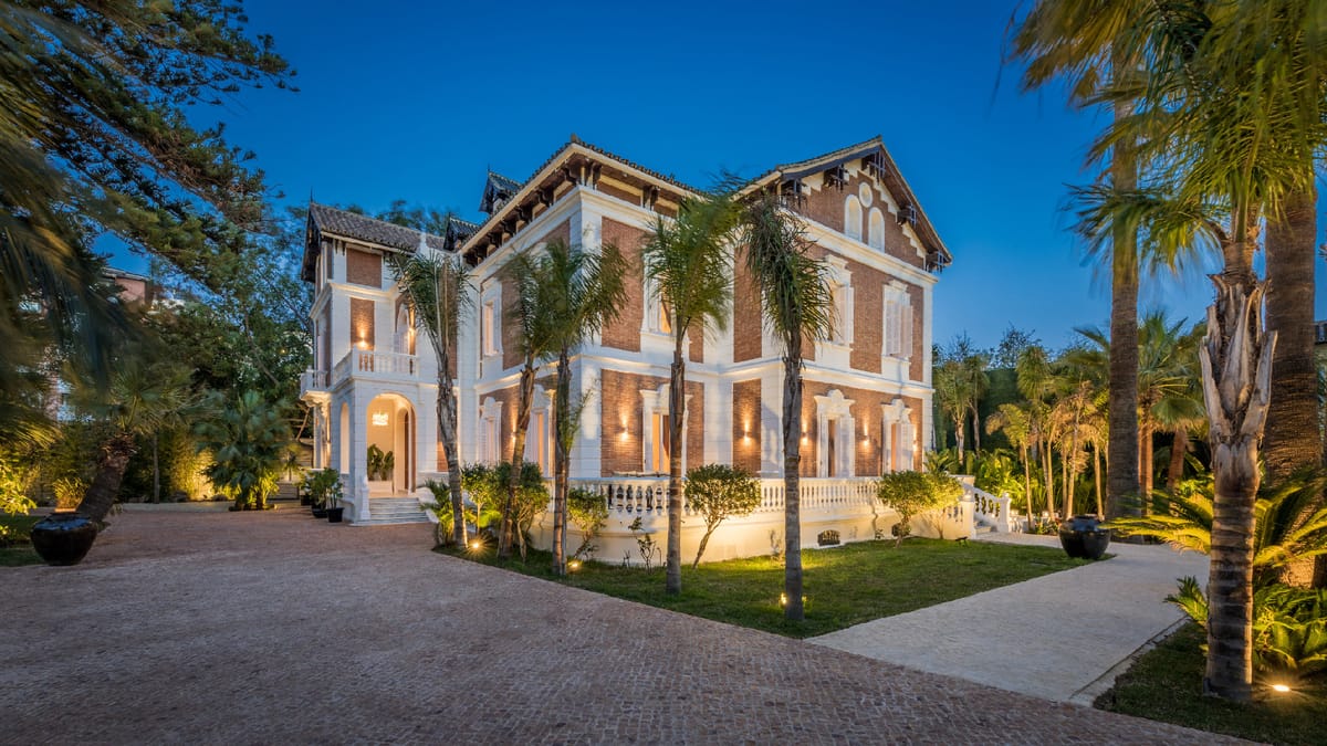 La fachada de ladrillo y estuco blanco del Palacio Limonar en la hora azul, con las luces del jardín encendidas entre palmeras